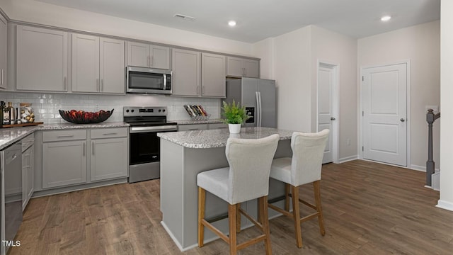 kitchen with gray cabinetry, a kitchen island, light stone countertops, and appliances with stainless steel finishes