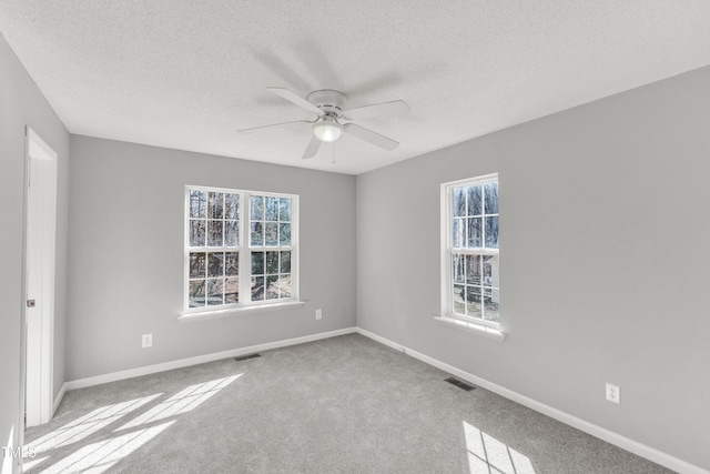 carpeted empty room with ceiling fan, a healthy amount of sunlight, and a textured ceiling