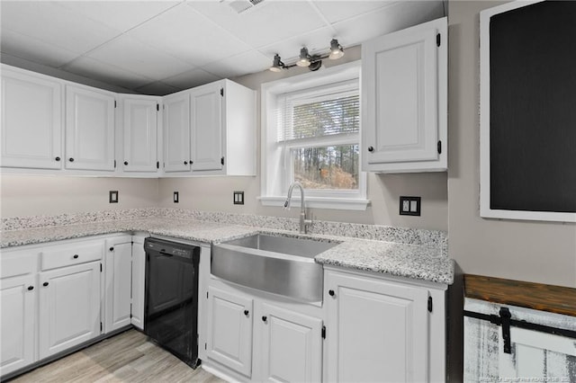 kitchen with light stone counters, black dishwasher, white cabinetry, a sink, and light wood-type flooring