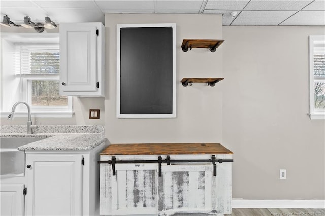 kitchen featuring light stone counters, a paneled ceiling, white cabinets, a sink, and baseboards