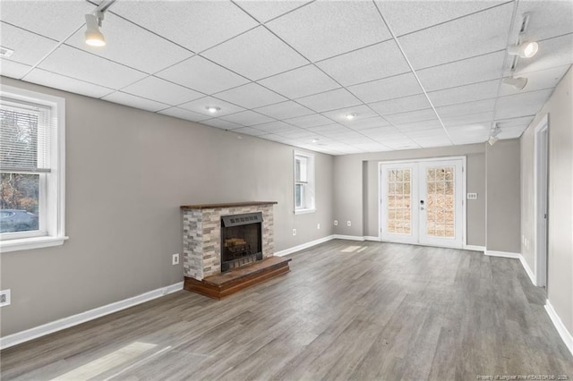 unfurnished living room with baseboards, a drop ceiling, wood finished floors, and a brick fireplace