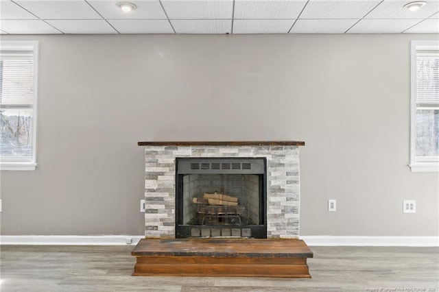 interior details featuring a paneled ceiling, baseboards, a fireplace with raised hearth, and wood finished floors