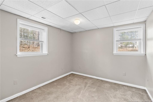 carpeted spare room with a healthy amount of sunlight, baseboards, and a drop ceiling