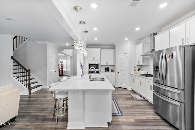 kitchen featuring sink, stainless steel appliances, wall chimney exhaust hood, white cabinets, and an island with sink