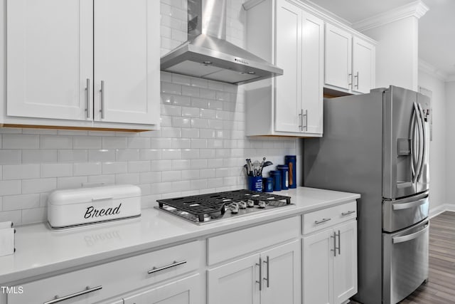 kitchen with appliances with stainless steel finishes, white cabinetry, wall chimney exhaust hood, ornamental molding, and decorative backsplash