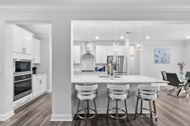 kitchen featuring white cabinets, appliances with stainless steel finishes, wall chimney exhaust hood, and a breakfast bar area