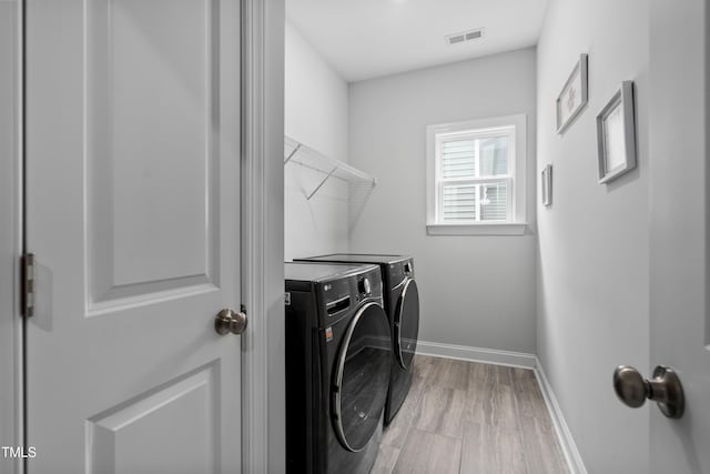 laundry area with independent washer and dryer and light hardwood / wood-style flooring