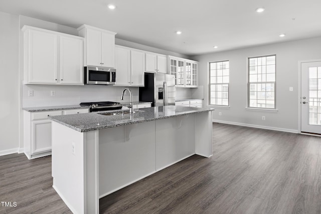 kitchen featuring sink, appliances with stainless steel finishes, a kitchen island with sink, white cabinetry, and dark stone countertops