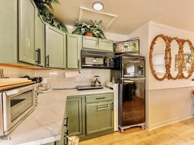 kitchen featuring backsplash, light stone counters, black appliances, light hardwood / wood-style floors, and green cabinetry