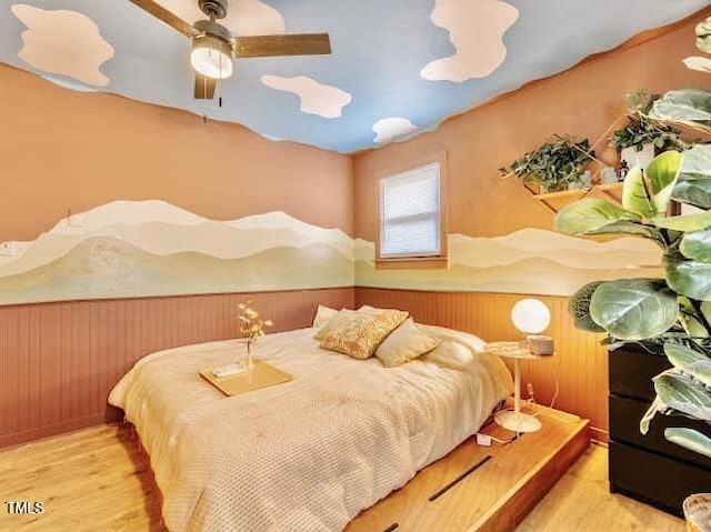 bedroom with ceiling fan, wooden walls, and light wood-type flooring