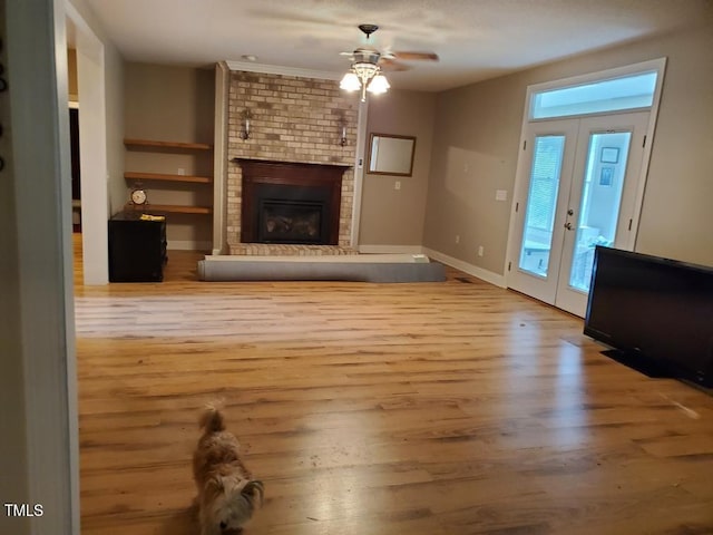 unfurnished living room with ceiling fan, a fireplace, wood finished floors, baseboards, and french doors