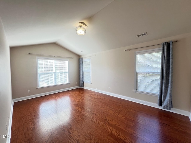 spare room featuring lofted ceiling, dark wood-type flooring, and plenty of natural light