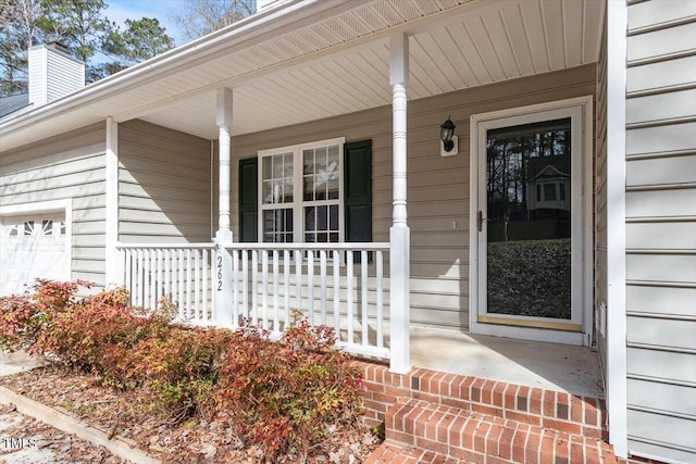 doorway to property featuring a porch, an attached garage, and a chimney