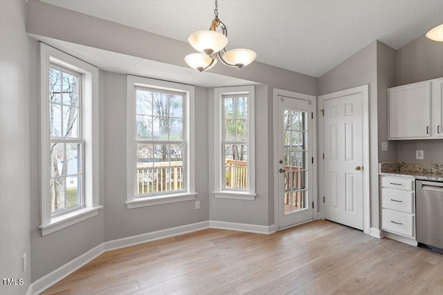 unfurnished dining area with lofted ceiling, an inviting chandelier, baseboards, and light wood finished floors