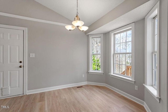 unfurnished dining area with visible vents, a notable chandelier, light wood-style flooring, baseboards, and vaulted ceiling