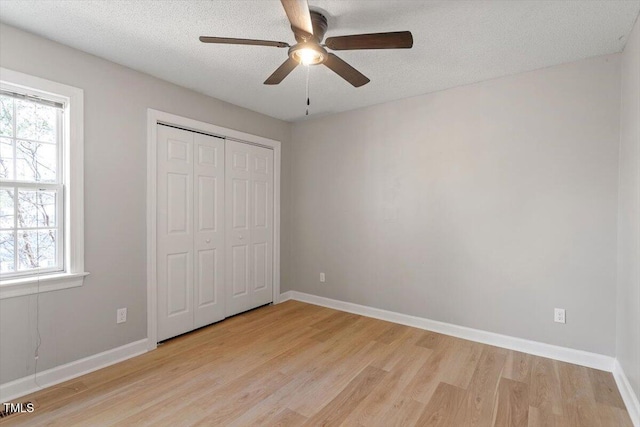 unfurnished bedroom featuring light wood finished floors, a closet, a textured ceiling, and baseboards