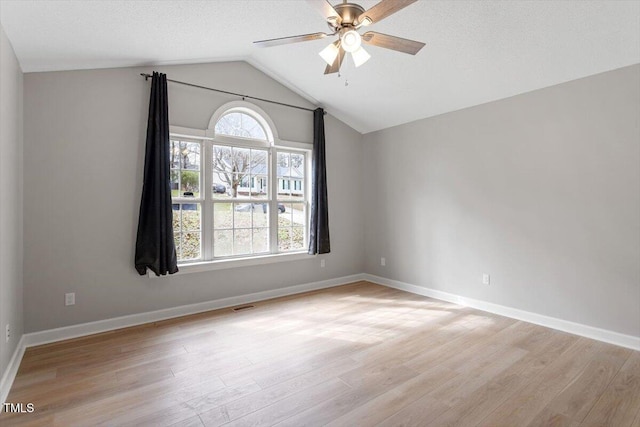 spare room with vaulted ceiling, light wood-style flooring, baseboards, and ceiling fan