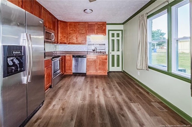 kitchen with crown molding, appliances with stainless steel finishes, hardwood / wood-style floors, and plenty of natural light