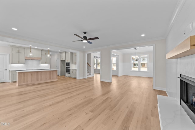 unfurnished living room with ceiling fan with notable chandelier, ornamental molding, and light hardwood / wood-style floors