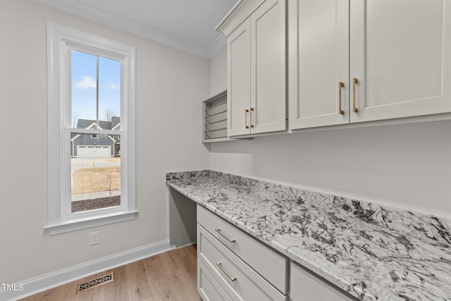 kitchen with built in desk, white cabinetry, light stone counters, crown molding, and light hardwood / wood-style flooring