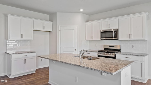 kitchen with appliances with stainless steel finishes, white cabinetry, sink, light stone counters, and a center island with sink