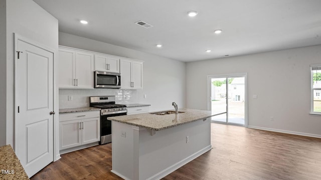 kitchen featuring appliances with stainless steel finishes, sink, white cabinets, dark wood-type flooring, and a center island with sink