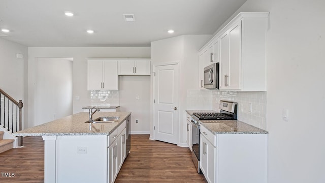 kitchen with sink, white cabinets, light stone counters, stainless steel appliances, and a center island with sink