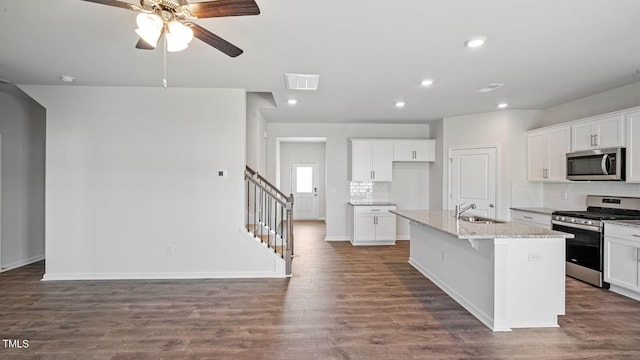 kitchen with an island with sink, sink, white cabinets, stainless steel appliances, and light stone countertops