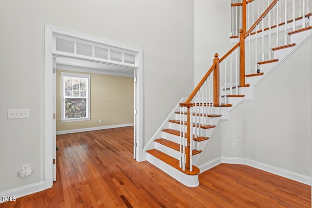 staircase featuring a towering ceiling, hardwood / wood-style flooring, and baseboards