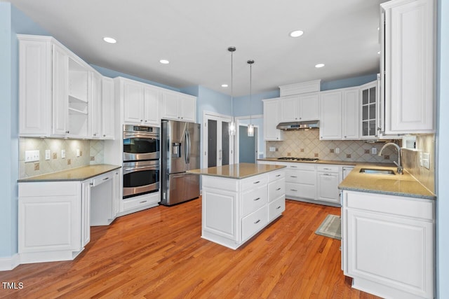 kitchen with light wood finished floors, white cabinets, stainless steel appliances, under cabinet range hood, and a sink