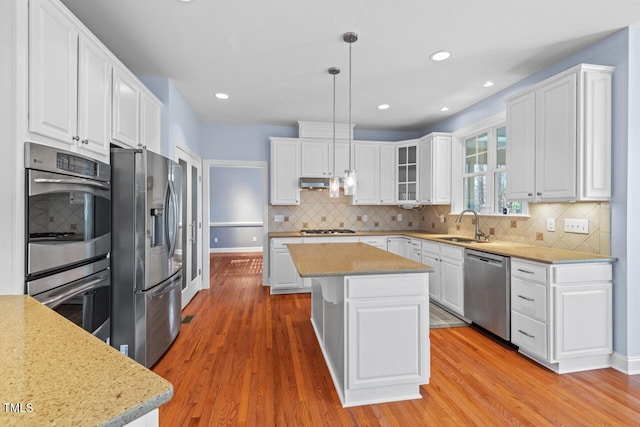 kitchen with appliances with stainless steel finishes, white cabinets, a sink, and light wood-style flooring