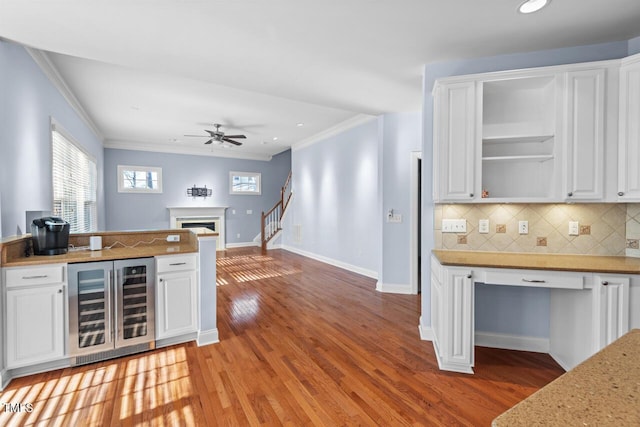 kitchen with beverage cooler, ornamental molding, light wood-type flooring, a fireplace, and white cabinetry