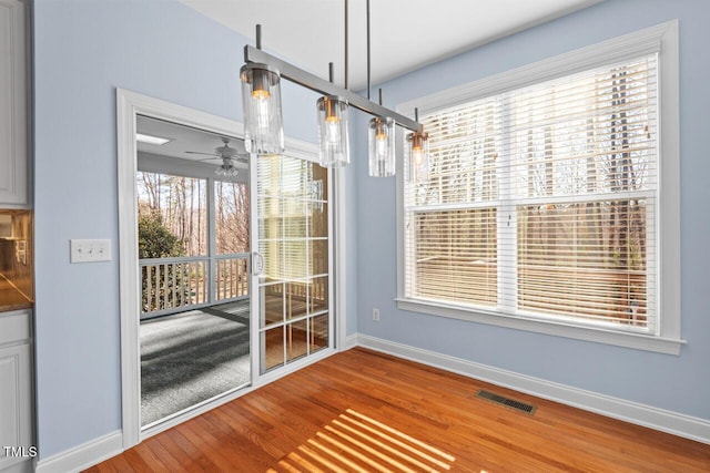 unfurnished dining area featuring baseboards, visible vents, wood finished floors, and ceiling fan with notable chandelier