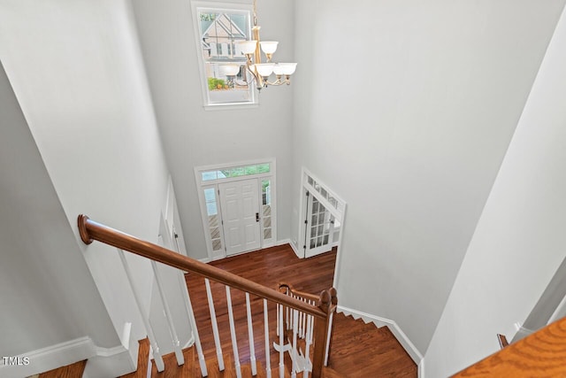 stairs with a chandelier, a towering ceiling, baseboards, and wood finished floors