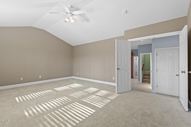 unfurnished bedroom featuring light carpet, baseboards, vaulted ceiling, and a ceiling fan