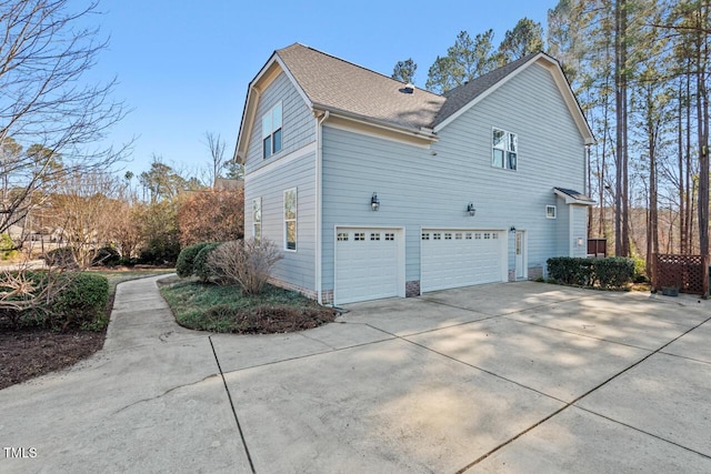 view of side of home featuring a garage, driveway, and roof with shingles