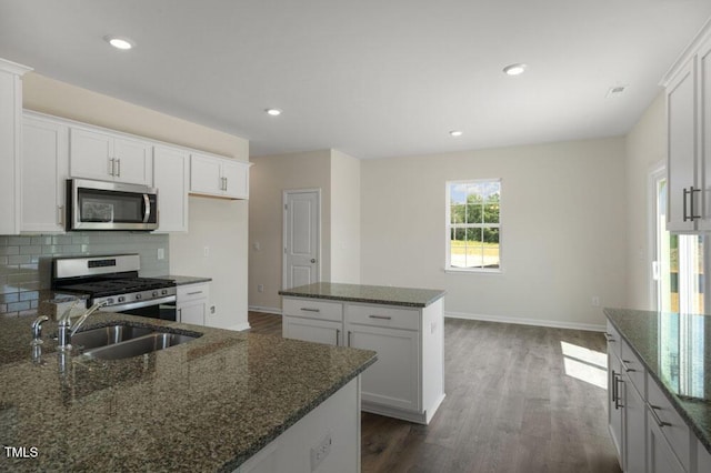 kitchen featuring stainless steel appliances, a center island, sink, and dark stone countertops