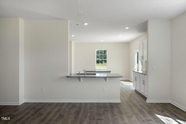 kitchen featuring light stone countertops, dark hardwood / wood-style floors, white cabinets, and a kitchen bar