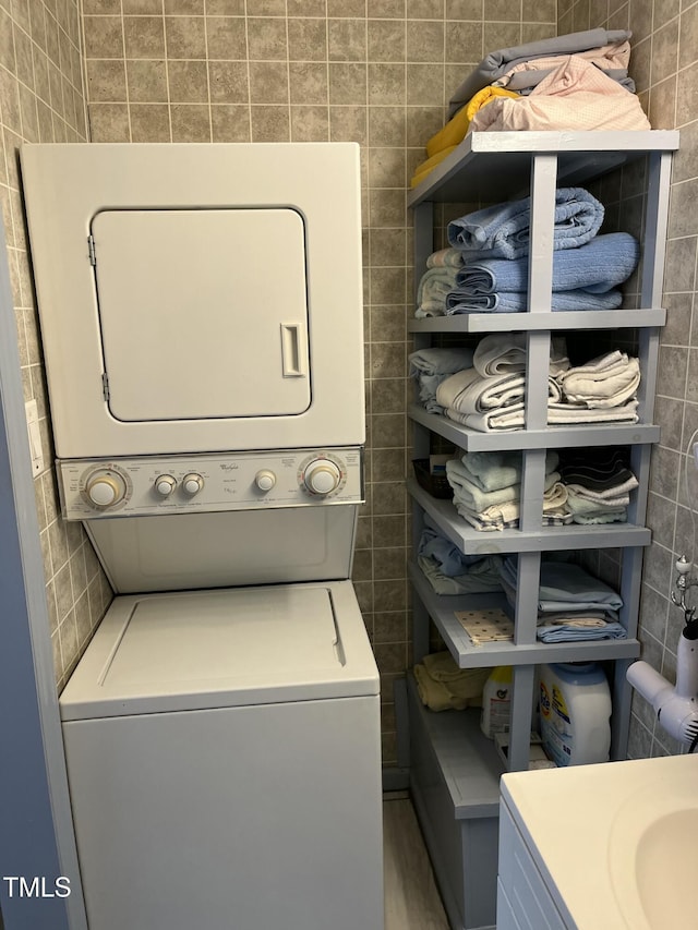 laundry room featuring stacked washing maching and dryer and tile walls