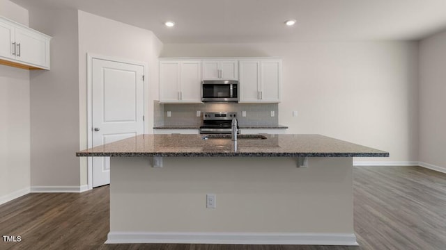 kitchen with appliances with stainless steel finishes, a kitchen island with sink, dark stone countertops, a kitchen breakfast bar, and white cabinets