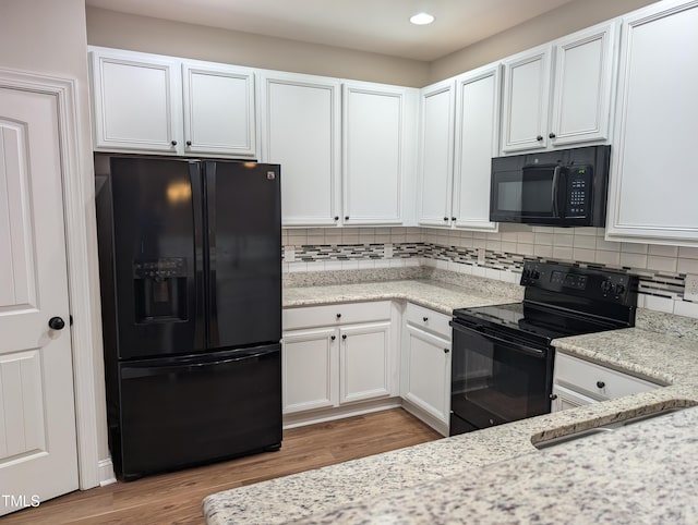 kitchen featuring white cabinetry, light stone countertops, decorative backsplash, and black appliances