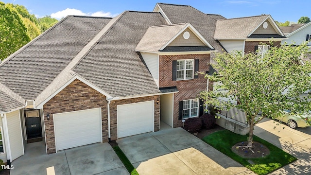 townhome / multi-family property featuring driveway, stone siding, brick siding, a garage, and a shingled roof