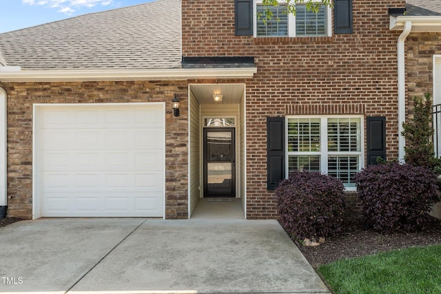 entrance to property featuring brick siding, roof with shingles, a garage, and concrete driveway