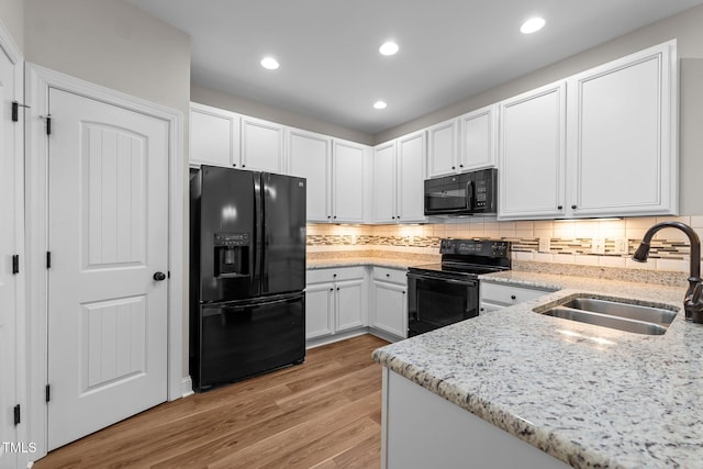 kitchen featuring light stone counters, a sink, black appliances, light wood-style floors, and white cabinetry