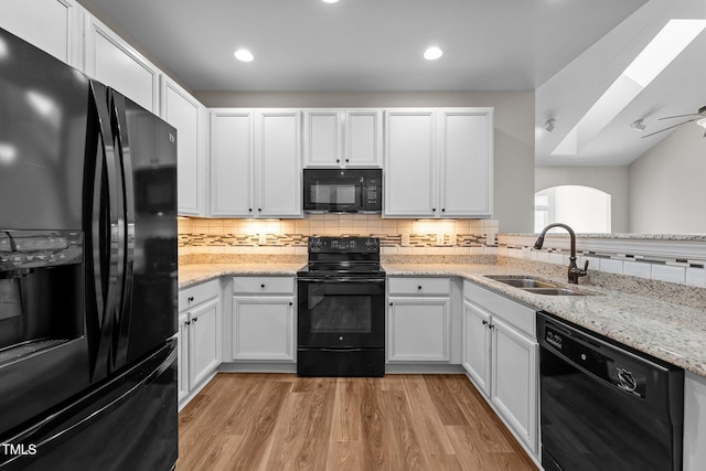 kitchen featuring backsplash, a sink, arched walkways, light wood-type flooring, and black appliances