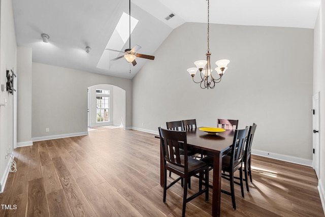 dining room featuring wood finished floors, arched walkways, baseboards, high vaulted ceiling, and ceiling fan with notable chandelier