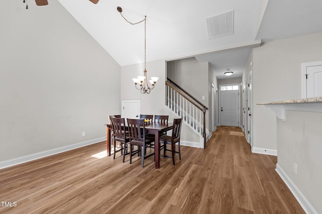 dining area featuring baseboards, visible vents, ceiling fan with notable chandelier, wood finished floors, and stairway