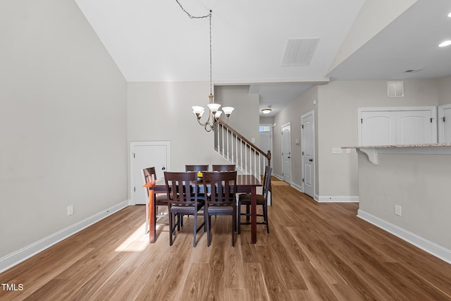 dining room featuring wood finished floors, visible vents, baseboards, and a notable chandelier