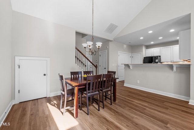 dining room featuring wood finished floors, visible vents, high vaulted ceiling, and a notable chandelier