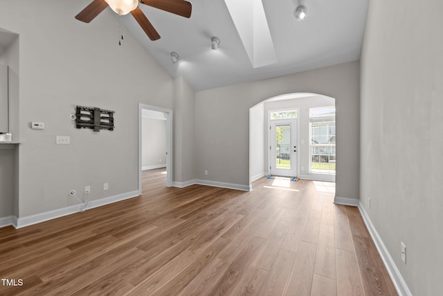 unfurnished living room featuring arched walkways, baseboards, wood finished floors, ceiling fan, and high vaulted ceiling